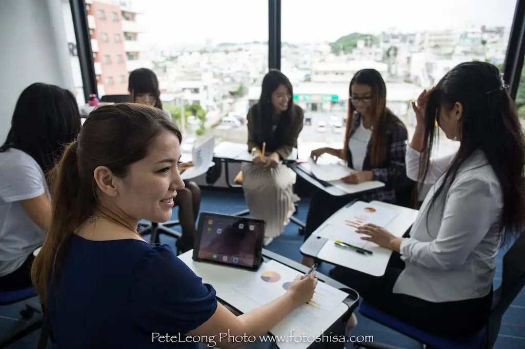 Japanese class is in session. A teachers teaches students sitting in a circle of chairs.